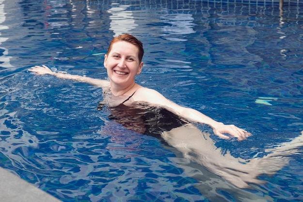 Middleaged woman swims in the pool and smiles