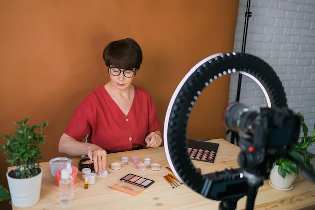 Middleaged woman talking on cosmetics with makeup eye shadows and blush palette and brushes while re