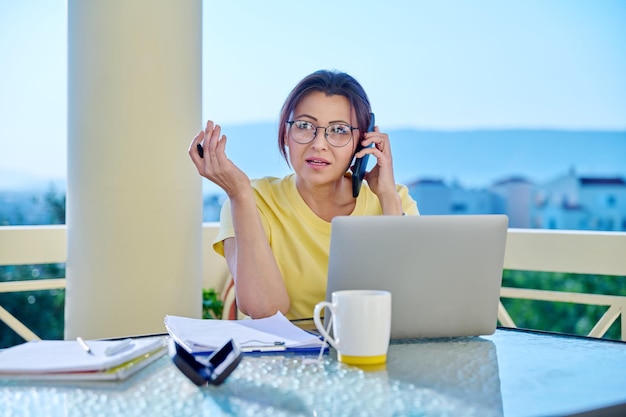 Middleaged woman working in home office on terrace talking on phone