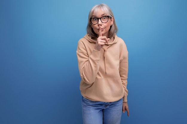 A middleaged woman in a youth outfit asks to be quieter on a studio background with copy space