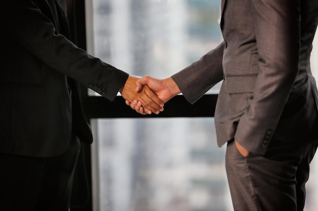 Midsection of colleagues handshaking while standing in office