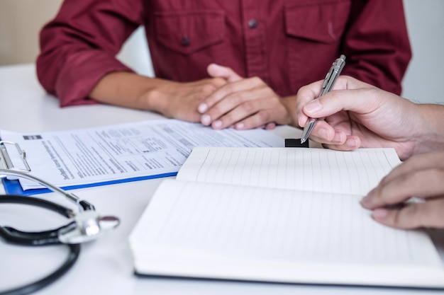 Midsection of doctor writing prescription while patient gesturing at hospital