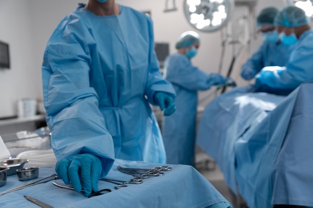 Midsection of female surgeon reaching for surgical scissors in operating theatre