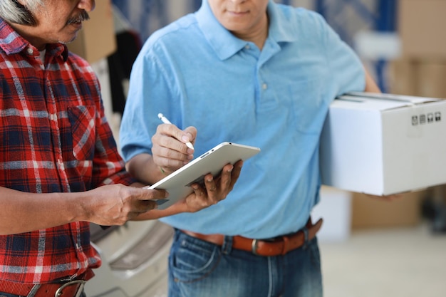 Photo midsection of man giving package to customer signing over digital tablet