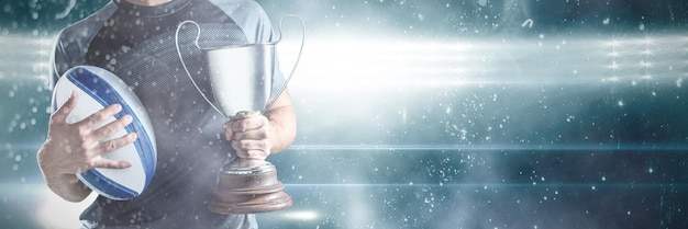 Midsection of successful rugby player holding trophy and ball