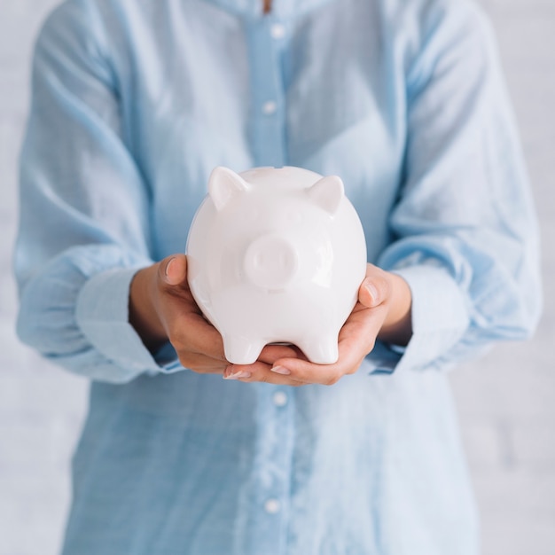 Midsection view of a woman's hand holding white piggybank