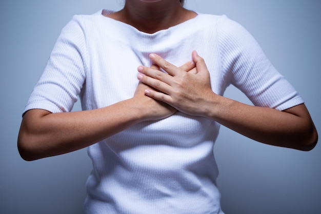 Midsection of woman touching chest in pain while standing against gray background