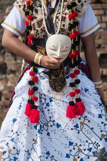 Photo midsection of woman in traditional clothing holding mask while standing against wall