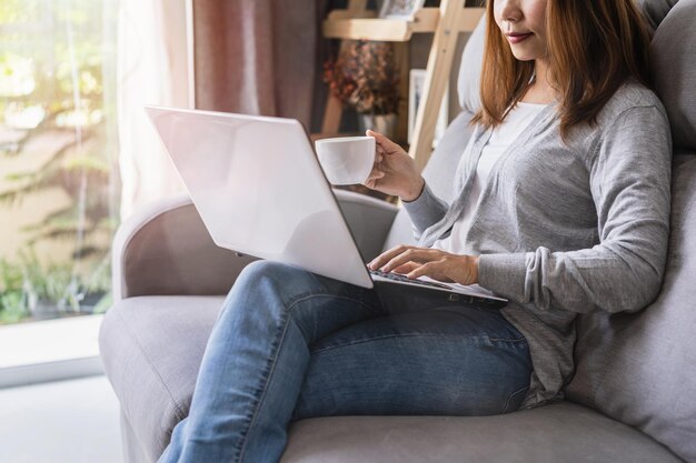 Midsection of woman using laptop while sitting on sofa at home