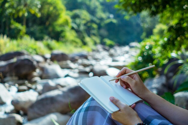 Photo midsection of woman writing in diary at forest