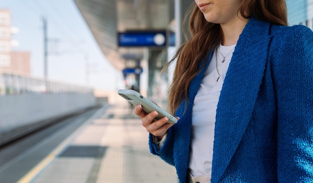 Midsection young stylish woman using mobile while waiting for train at station public transport high