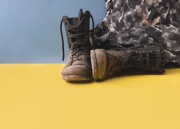 Military dirty combat boots next to a bulletproof vest on a yellow blue background conflict in Ukraine a place for text