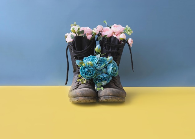 Military dirty combat boots with flowers on a yellow blue background conflict in Ukraine place for text