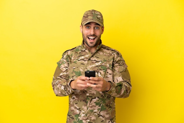 Military man isolated on yellow background surprised and sending a message