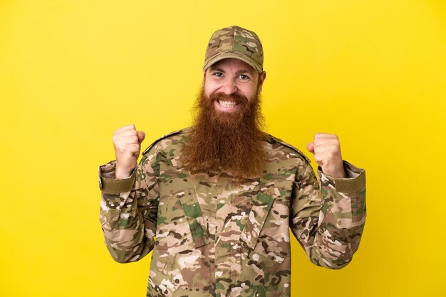 Photo military redhead man over isolated on yellow background celebrating a victory in winner position