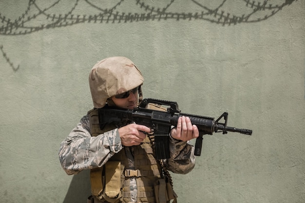 Military soldier aiming with a rifle against concrete wall in boot camp