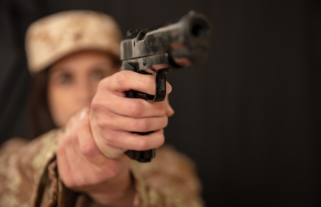 Military woman with a gun in hand aiming at camera Female soldier in army uniform