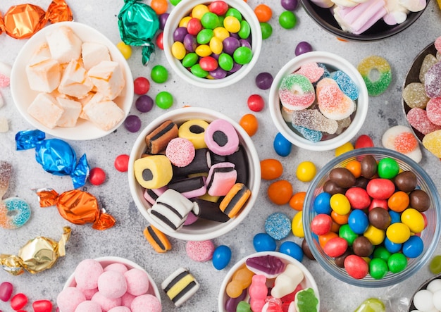 Milk chocolate candies woth shell in jar with various jelly gums candies on white table with liquorice allsorts and strawberry bonbons with different sour sugar gums