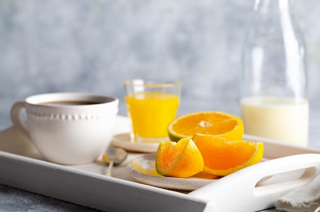 Milk a cup of coffee orange juice and pieces of orange in a white tray and grey background