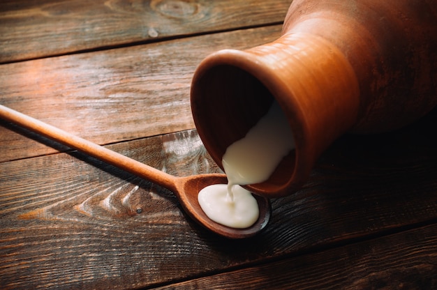 Milk flows from a clay jug on brown wooden surface