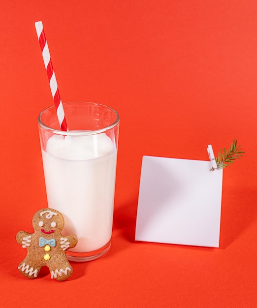 Milk glass with drinking straw gingerbread man and empty white note on red Milk for Santa Mock up