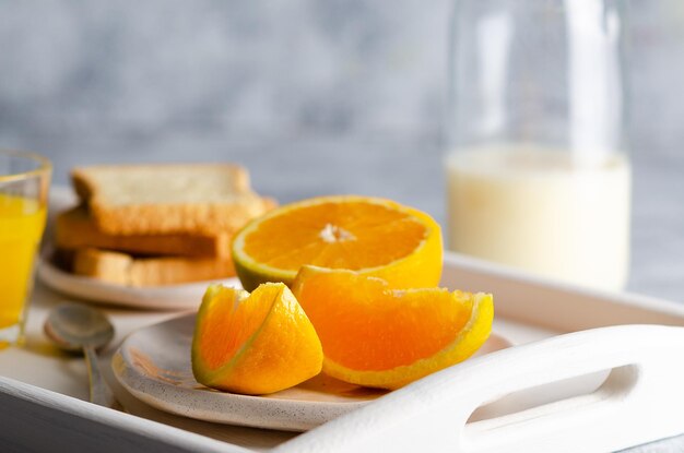 Milk orange juice and pieces of orange in a white tray and grey background