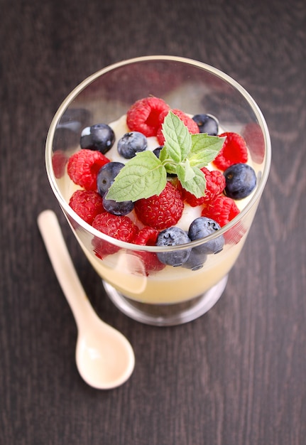 Milk pudding with berries in a glass on a black background