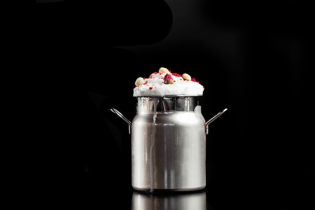 Milkshake with foam in metallic jar isolated on black background.