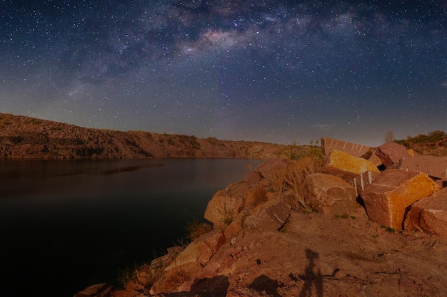 Milky Way over a lake in a granite quarry at night Summer landscape with huge boulders trees purple sky with milky way and stars beautiful reflection in the water Ukraine Space and nature