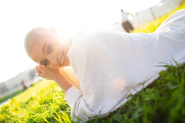 Millenial young woman blonde short hair outdoor smiling lay on grass portrait.