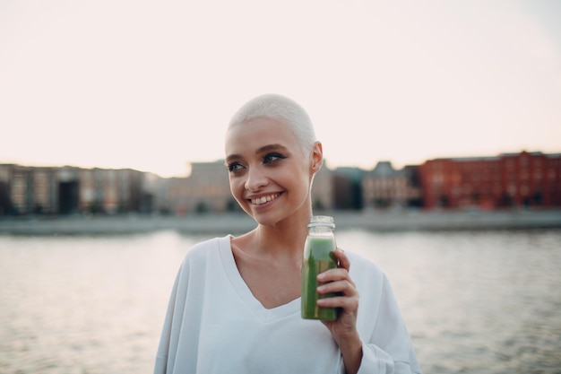 Millenial young woman blonde short hair outdoor with green smoothie