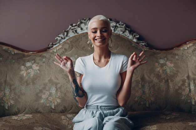 Millenial young woman with short blonde hair portrait sitting and meditate with ok sign mudra on vin...