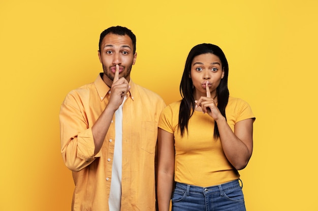 Millennial african american guy and female putting finger to mouth making shhh sign