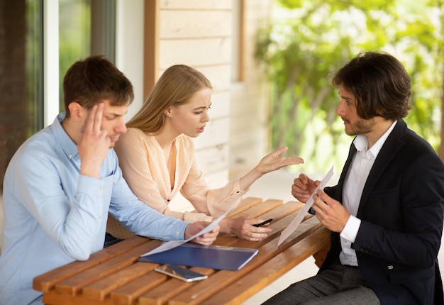 Millennial family disappointed at bad rental terms and property manager at table on house porch