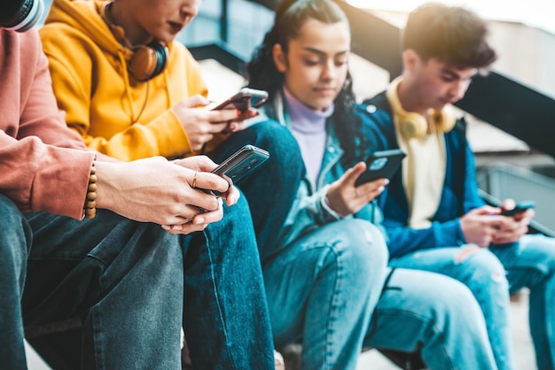 Millennial friends watching smart mobile phone device outside Young people using cellphones playing on social media platforms Technology addiction concept