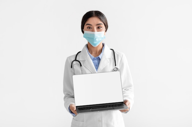 Millennial hindu woman in coat show laptop with empty screen isolated on white background