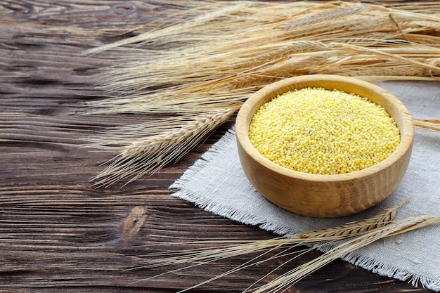 Millet in a bowl and wheat ears on a brown wooden table