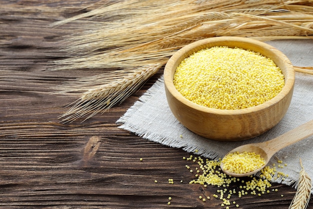 Millet in a bowl and wheat ears on a brown wooden table