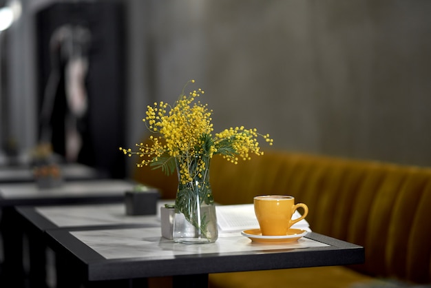 mimosa in a vase and coffee in a yellow cup on a table in a cafe or restaurant.