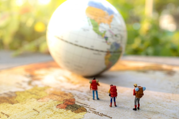 Minature people: traveling with a backpack standing on vintage world map, Travel and summer concept.