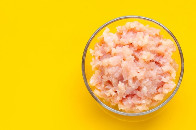 Minced meat of chicken fillet in glass bowl on yellow background.