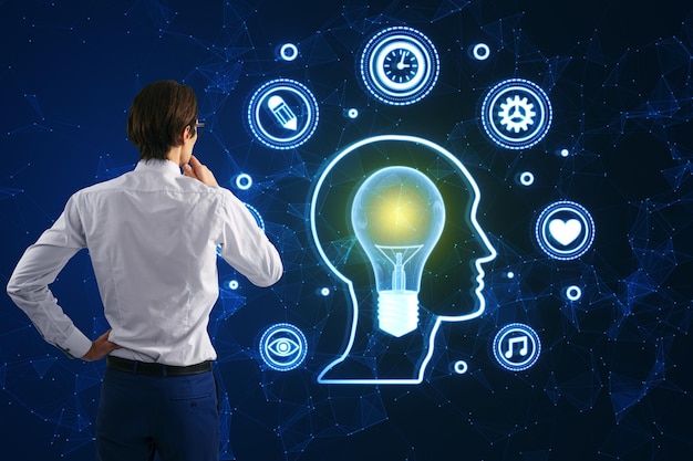 Mind mapping and creative inspiration concept Back view of young man looking at glowing head outline with digital lamp and other polygonal icons on blurry blue background