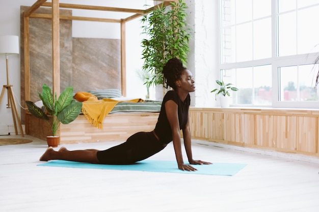 Mindful dark skin african american woman with close eyes do yoga exercises indoors Relax and stretching in cobra pose