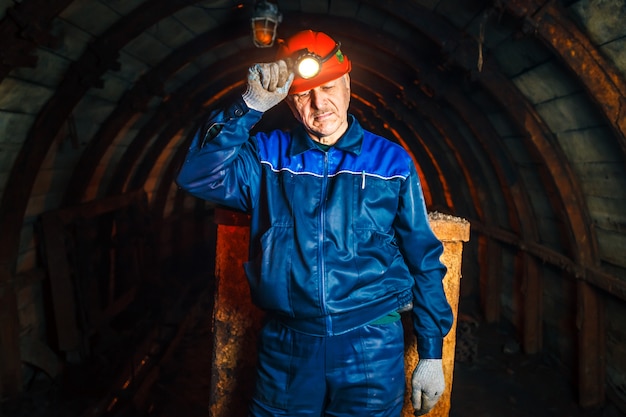 A miner in a coal mine stands near a trolley. Copy space.