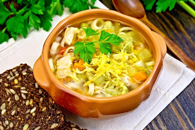 Minestrone soup with meat celery tomatoes zucchini and cabbage green peas carrots and pasta in an earthenware bowl cheese bread on a dark wooden board