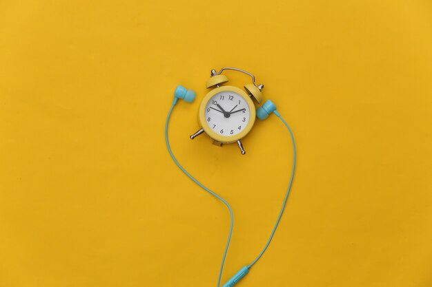 Mini alarm clock and earphones on yellow background.