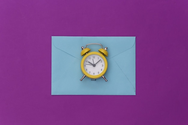 Mini alarm clock and envelopes on a purple background.