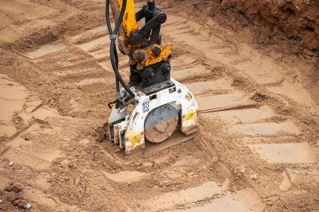 Photo a mini excavator rams the ground with a vibrating plate laying of underground sewer pipes and communications during construction soil compaction earthworks excavation