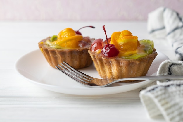 Mini fruit tarts with orange cherry and kiwi on white plate.