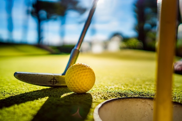 Mini Golf yellow ball with a bat near the hole at sunset